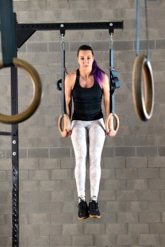 Young woman athlete doing muscle up exercises on rings during her workout in the gym in a full length frontal view raised on extended arms