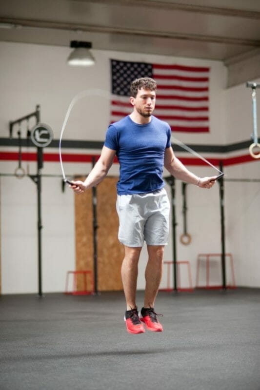 Fit athletic young man using a skipping rope to train in a crossfit gym jumping midair in a health and fitness concept