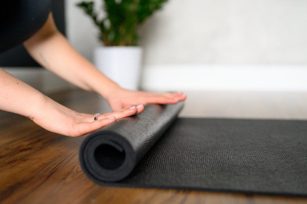 A Woman Rolls Up A Yoga Mat After A Workout In The Studio